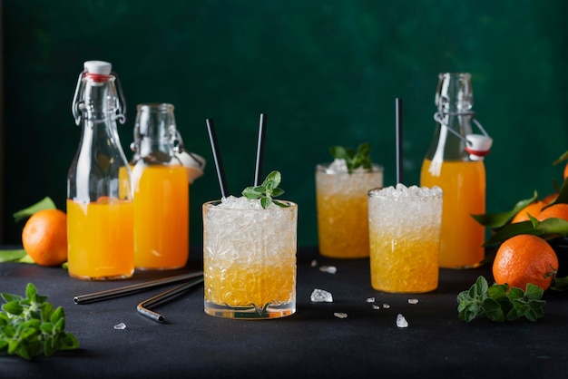 Concept de bar : cocktail avec des mandarines fraîches, de la glace pilée et des feuilles de menthe sur fond sombre, image de mise au point sélective