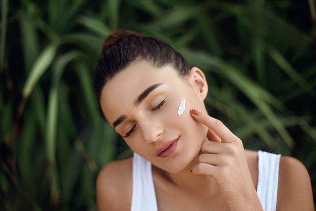 Concept de beauté Belle femme modèle avec crème hydratante sur le visage Portrait de jeune fille en tropical