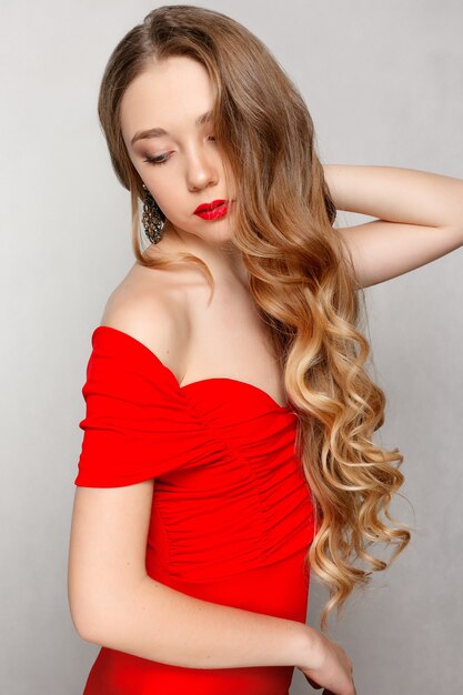 Concept de beauté, de coiffure et de personnes - Belle brune modèle aux longs cheveux bouclés. Fille grand collier perles et chaîne. Bijoux et accessoires .Coiffure boucles ondulées. fille en robe rouge et bijoux