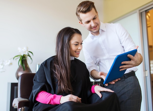 concept beauté, coiffure, technologie et personnes - heureuse jeune femme et styliste avec tablette pc au salon