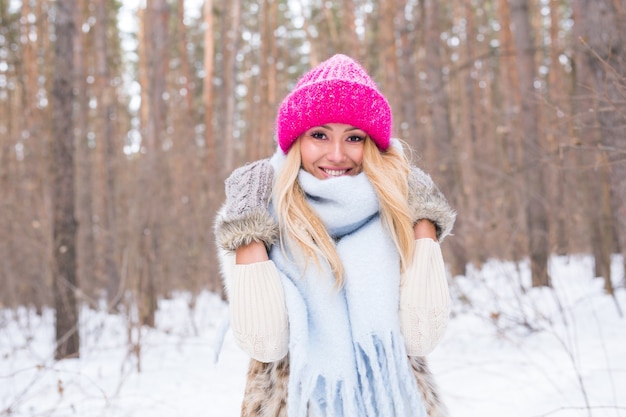 Concept de beauté, hiver et personnes - Jolie femme blonde dans un pull rose dans la forêt enneigée est