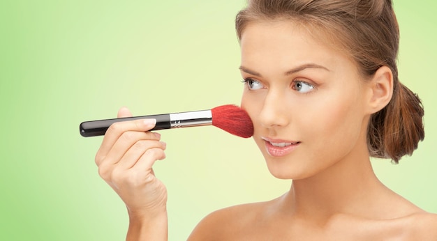 Photo concept de beauté, de personnes et d'accessoires - belle femme souriante aux épaules nues et pinceau de maquillage sur fond vert