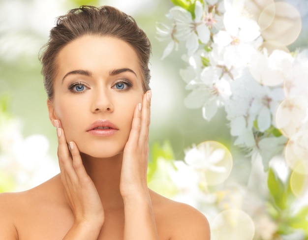 concept de beauté, de personnes, d'été, de printemps et de santé - belle jeune femme touchant son visage sur fond de jardin fleuri vert