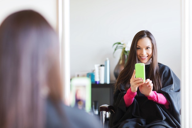 concept de beauté et de personnes - jeune femme heureuse avec un smartphone prenant un selfie miroir au salon de coiffure