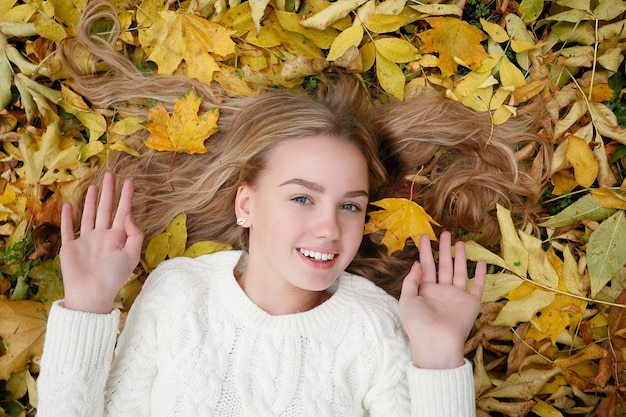 Concept de beauté, de personnes, de saison et de santé - la jolie fille est allongée dans les feuilles d'automne jaunes