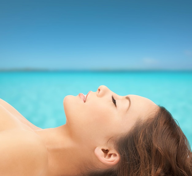 concept de beauté, de personnes et de santé - belle jeune femme allongée les yeux fermés sur fond bleu ciel et mer