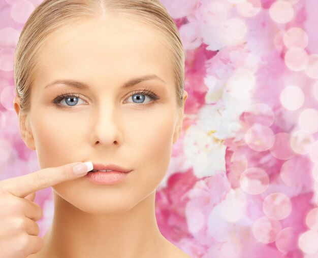 concept de beauté, de personnes et de santé - belle jeune femme pointant le doigt vers ses lèvres sur fond floral rose
