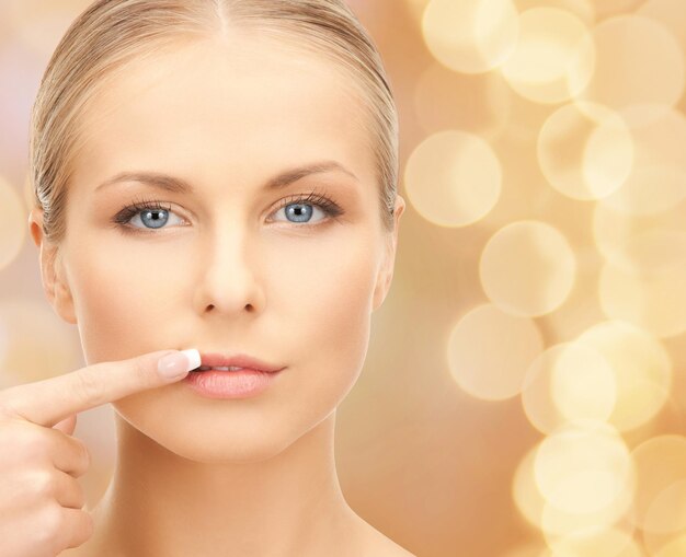 concept de beauté, de personnes et de santé - belle jeune femme pointant le doigt vers ses lèvres sur fond de lumières beiges