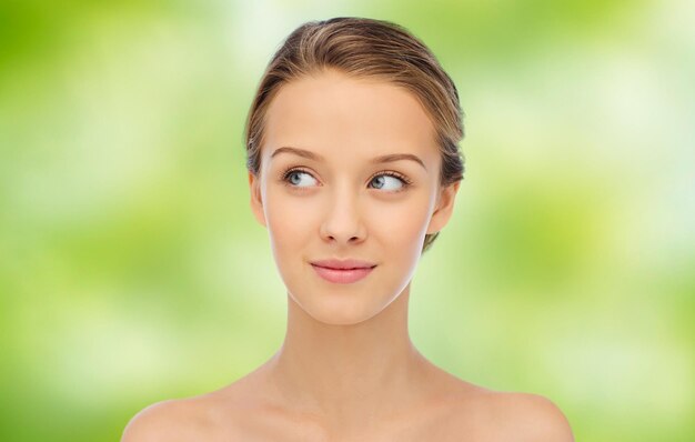 concept de beauté, de personnes et de santé - jeune femme souriante visage et épaules sur fond naturel vert