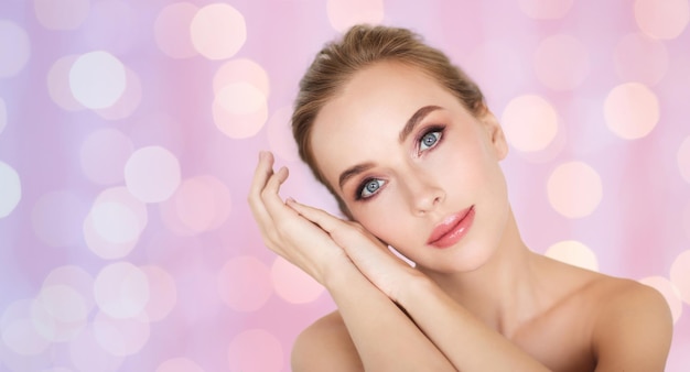 concept de beauté, de personnes et de soins du corps - beau visage de jeune femme et mains sur fond de lumières de quartz rose et de sérénité