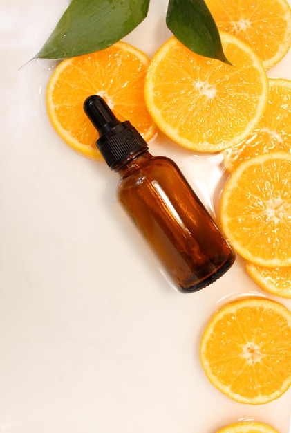 Concept de beauté de sérum de vitamine C dans une bouteille cosmétique avec compte-gouttes et tranches de fruits orange sur fond blanc.