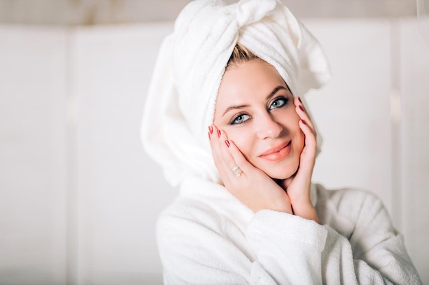 Concept beauté et spa. Gros plan d'une jeune femme heureuse appliquant une crème hydratante sur son visage, touchant le visage en profitant d'une peau douce et fraîche après les procédures de spa regardant avec un joli sourire à la caméra.