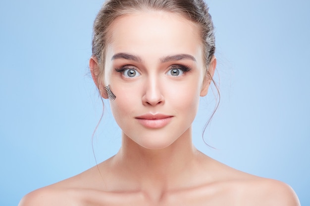 Concept de beauté, tête et épaules de jeune femme avec un maquillage naturel. Gros plan d'une fille regardant la caméra avec de faux cils collés sur la joue, yeux arrondis