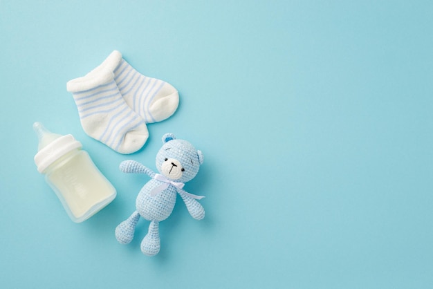 Concept bébé garçon vue de dessus photo de petites chaussettes bouteille de lait et jouet ours en peluche tricoté sur fond bleu pastel isolé