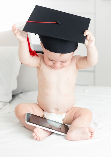 Concept de bébé intelligent. Mignon petit garçon en chapeau de graduation navigation sur internet sur tablette numérique