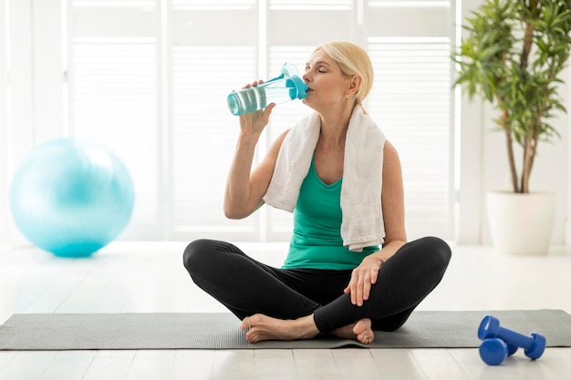 Concept de bien-être femme mûre sportive buvant de l'eau après l'entraînement à la maison