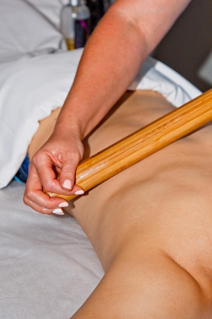 Concept de bien-être Un masseur professionnel donne à un homme un massage thaïlandais avec des bâtons de bambou au spa Détente et récupération après le travail