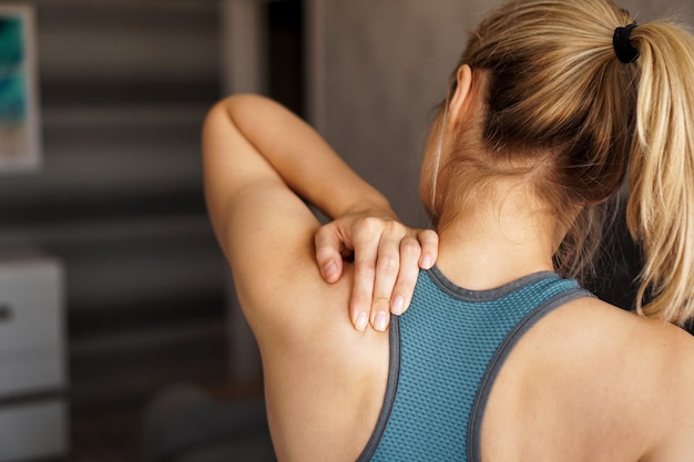 Concept de blessure sportive. Fille athlétique ressentant de la douleur dans son cou contre floue. Douleur après l'entraînement à domicile