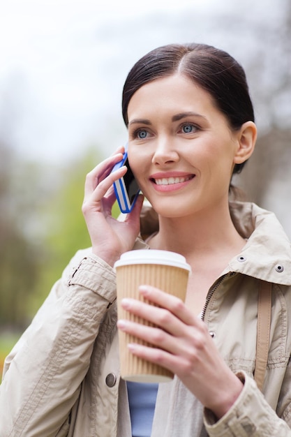 concept de boissons, de loisirs, de technologie et de personnes - femme souriante avec un café appelant et parlant sur un smartphone dans le parc