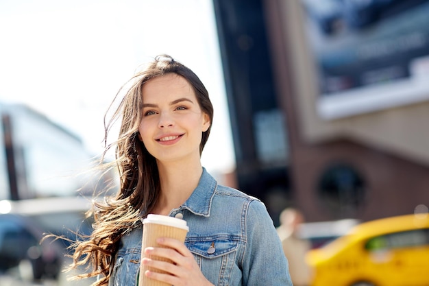 concept de boissons et de personnes - heureuse jeune femme ou adolescente buvant du café à partir d'une tasse de papier dans la rue de la ville