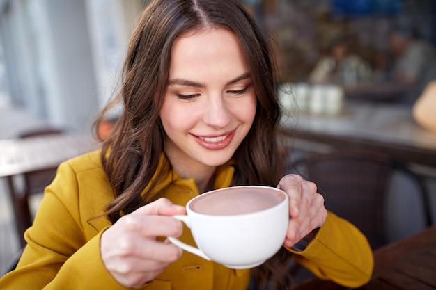 concept de boissons et de personnes - heureuse jeune femme ou adolescente avec une tasse buvant un délicieux cacao à la terrasse du café de la rue de la ville