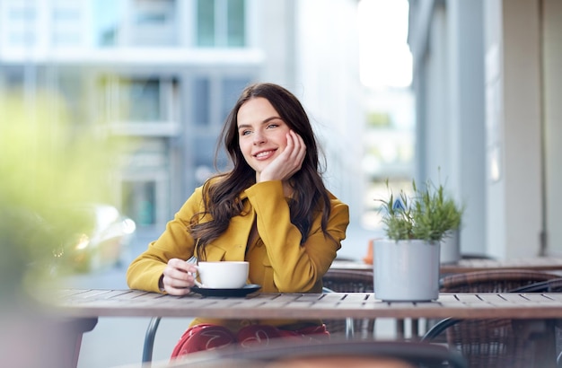 concept de boissons et de personnes - heureuse jeune femme ou adolescente avec une tasse buvant du cacao à la terrasse du café de la rue de la ville et rêvant