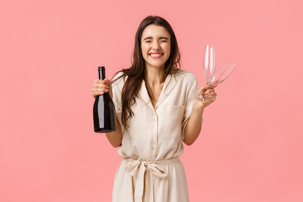 Concept de bonheur, de célébration et de félicitations. Charmante et excitée, extatique femme caucasienne en robe, fermer les yeux et sourire joyeusement, bouteille de champagne ouverte et boire ensemble