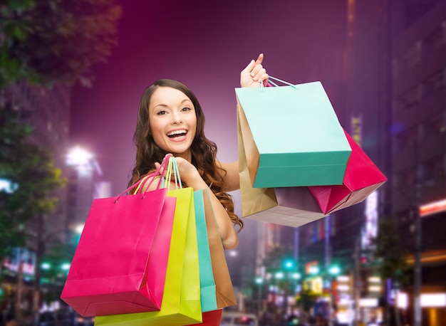 concept de bonheur, de consommation, de vente et de personnes - jeune femme souriante avec des sacs à provisions sur fond de ville nocturne
