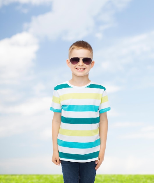 concept de bonheur, d'été, d'enfance, de nature et de personnes - petit garçon mignon souriant à lunettes de soleil sur fond naturel