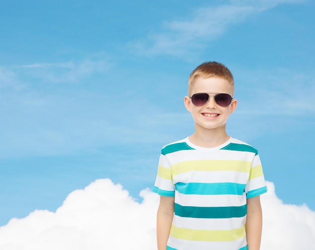 concept de bonheur, d'été, d'enfance et de personnes - sourire mignon petit garçon à lunettes de soleil sur fond de ciel bleu