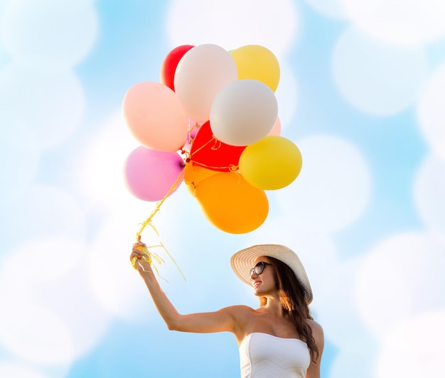 concept de bonheur, d'été, de vacances et de personnes - jeune femme souriante portant des lunettes de soleil avec des ballons sur fond de lumières bleues