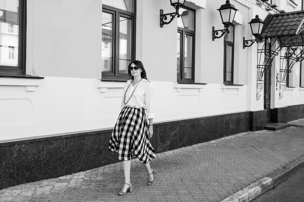 Concept de bonheur - femme heureuse s'amuser sur la rue de la ville. Femme Fashion à lunettes de soleil marche dans la rue sur des talons hauts. Image en noir et blanc.