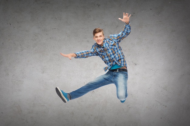 Photo concept de bonheur, de liberté, de mouvement et de personnes - jeune homme souriant sautant dans l'air sur fond de mur en béton