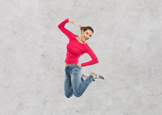 concept de bonheur, de liberté, de puissance, de mouvement et de personnes - jeune femme souriante sautant dans l'air avec le poing levé sur fond de mur de béton gris