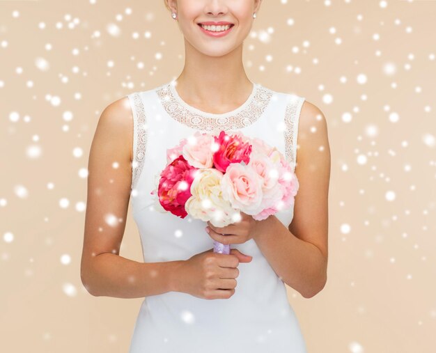 concept de bonheur, de mariage, de vacances et de célébration - gros plan d'une mariée ou d'une demoiselle d'honneur souriante en robe blanche avec bouquet de fleurs sur fond beige et neige