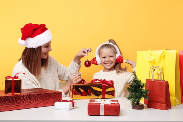 Concept de bonne année. Heureuse mère avec enfant s'amusant ensemble assis au bureau avec des cadeaux.