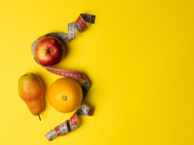 Le concept de bonne nutrition. Fruits juteux, ruban à mesurer enveloppé d'orange poire pomme sur fond jaune vif. Vue de dessus, espace de copie