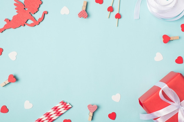 Concept de bonne Saint Valentin. Photo ci-dessus image de décorations rouges et blanches petit paquet enveloppé de cupidon et épingles coeur sur fond clair avec un espace vide