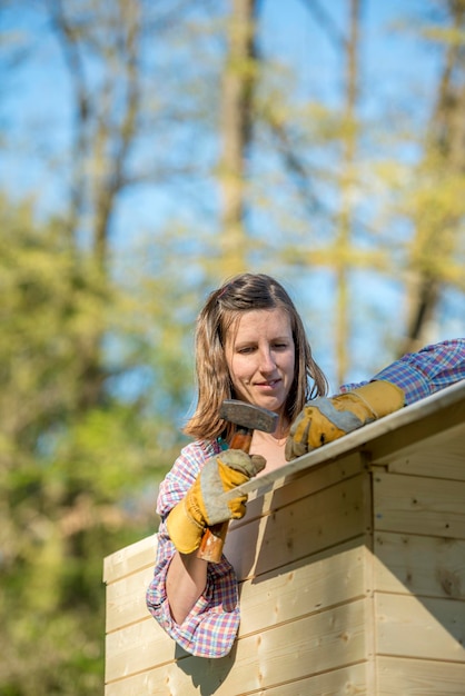 Concept de bricolage jeune femme tenant un marteau travaillant sur une maisonnette en bois