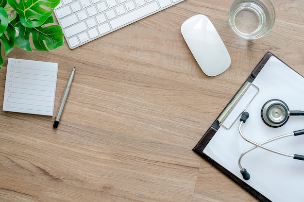 Concept de bureau de travail de médecin, clavier blanc, souris, graphique et stéthoscope sur table en bois.