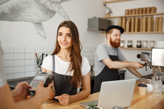 Concept Business Café - Belle femme barista offrant un service de paiement pour client avec carte de crédit et souriant en travaillant au comptoir bar dans un café moderne.