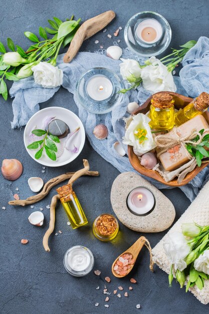 Concept de cadre de bien-être nature morte au spa Assortiment d'huiles essentielles crème sel de mer bougies de savon naturel fleurs printanières blanches et serviette sur un tableau noir Vue de dessus à plat