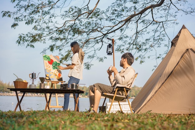 Concept de camping Jeune couple faisant une activité à l'extérieur de la tente pour peindre sur toile et boire du café