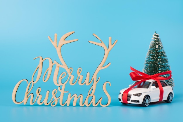 Concept De Carte Postale Joyeux Noël. Photo Photo De La Voiture Actuelle Avec Un Sapin à Ruban Et Un Texte De Félicitation D'invitation Isolé Sur Fond Bleu