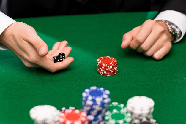 concept de casino, de jeu, de poker, de personnes et de divertissement - gros plan sur un joueur de poker avec des dés et des jetons à la table de casino verte