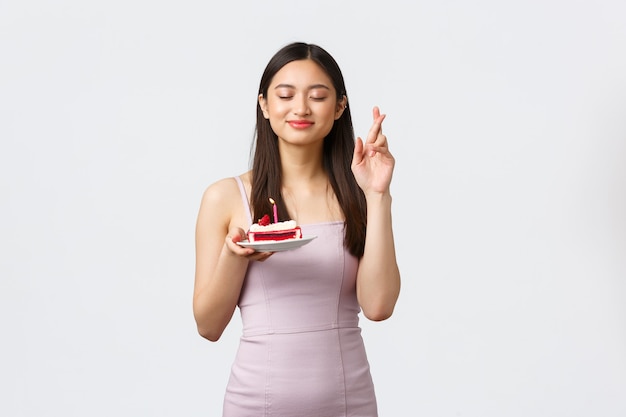 Concept de célébration, fête et vacances. Heureux rêveur belle femme asiatique en robe, croiser les doigts bonne chance avec les yeux fermés