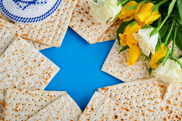 Concept de célébration de la Pâque Étoile bleue de David à base de matzah roses blanches et jaunes kippa et noix sur fond bleu Rituel traditionnel Nourriture juive de la Pâque Fête juive de Pessa'h Maquette