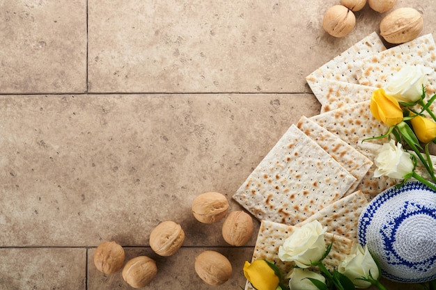 Concept de célébration de la Pâque Matzah casher vin rouge noyer et roses blanches et jaunes Pain juif rituel traditionnel sur fond de mur de tuiles anciennes de couleur sable Nourriture de la Pâque Fête juive de Pessah