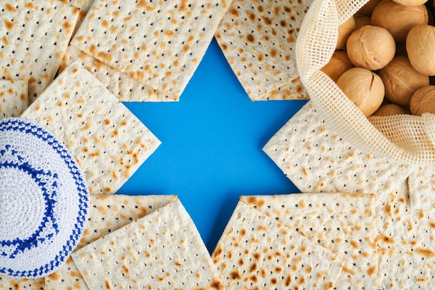 Concept de célébration de la Pâque Étoile bleue de David à base de matzah roses blanches et jaunes kippa et noix sur fond bleu Rituel traditionnel Nourriture juive de la Pâque Fête juive de Pessa'h Maquette