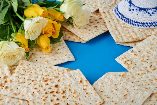 Concept de célébration de la Pâque Étoile bleue de David à base de matzah roses blanches et jaunes kippa et noix sur fond bleu Rituel traditionnel Nourriture juive de la Pâque Fête juive de Pessa'h Maquette